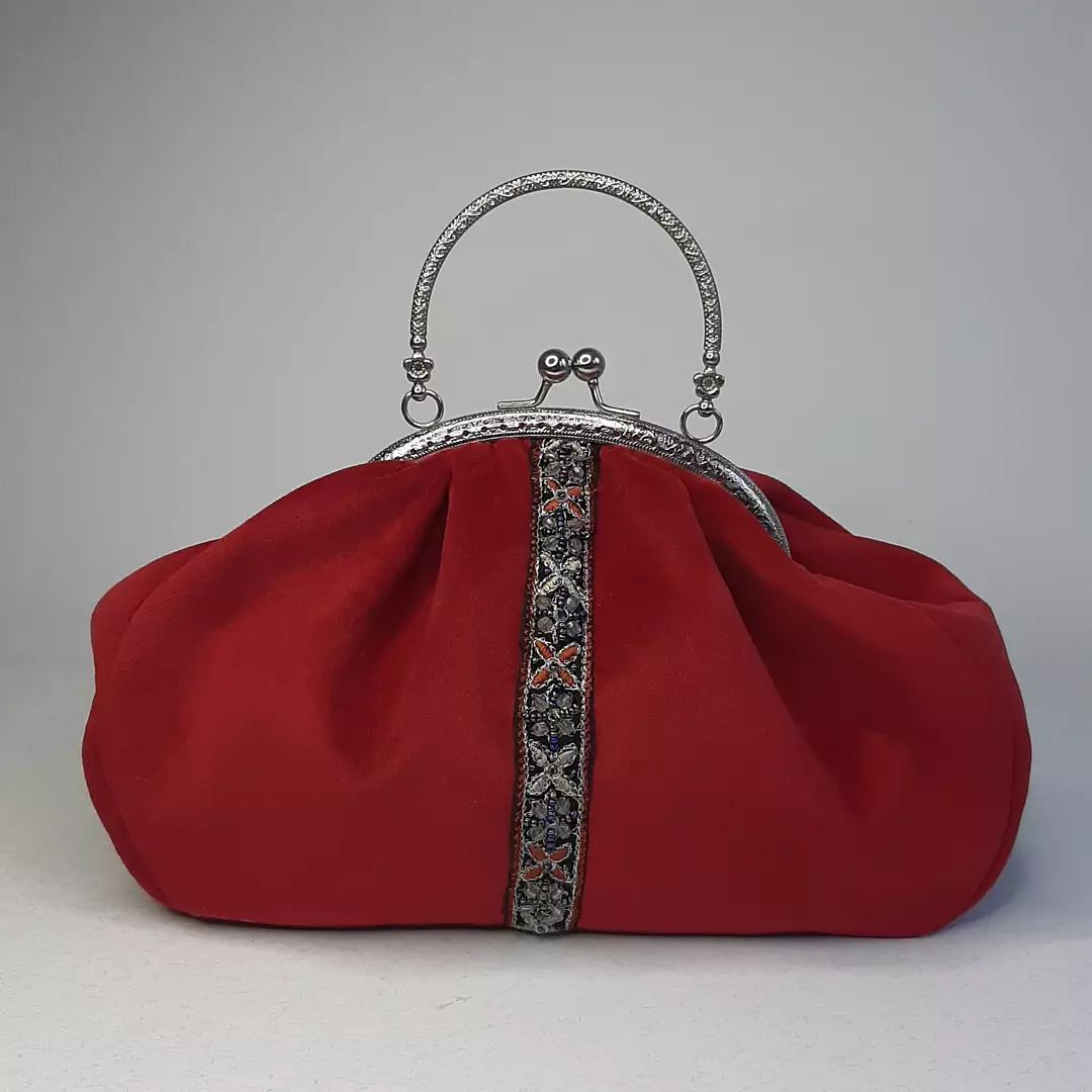 red suede purse with x shaped flower patterns in grey and red and silver handle